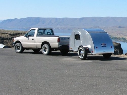 A white pickup truck pulling a small silver teardrop camper. 