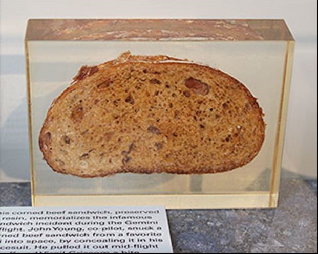 A corned beef sandwich, preserved in resin, standing vertically on display. 