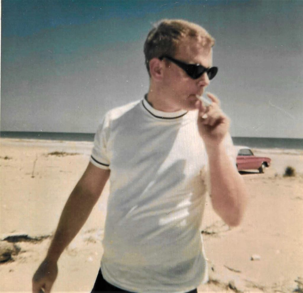 Michael Hudgens on a beach in the sunshine, looking away from the camera. 