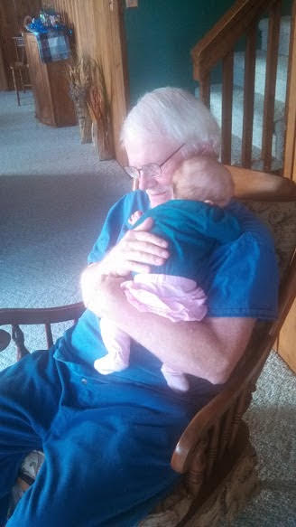 Michael Hudgens in a rocking chair holding a tiny baby closely. 