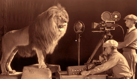 Image of a lion next to a microphone and two men running a sound system. 