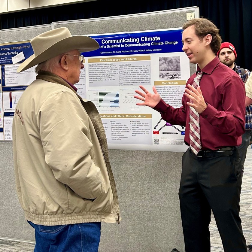 Colin Gholson presenting to an audience member in front of his poster. 