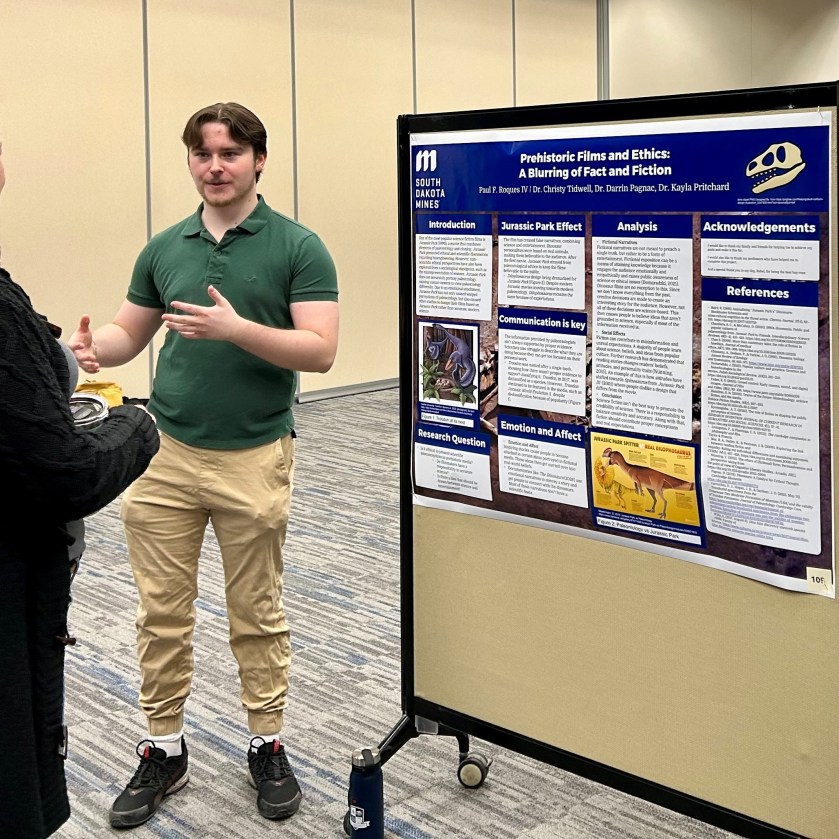 Paul Roques standing next to his poster, presenting to an audience member. 