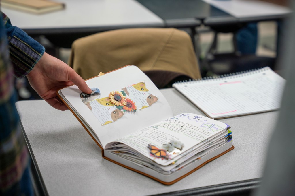 A commonplace book is opened to show off interior pages that include writing, stickers, and images.