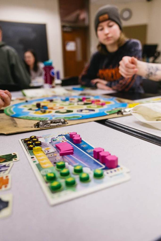 The foreground features game resources, with students playing in the background. 
