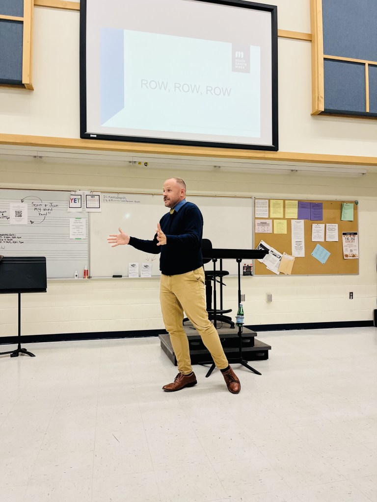 Dr. Gerrit Scheepers in the classroom as a conductor, with his hands out in a gesture in front of him.